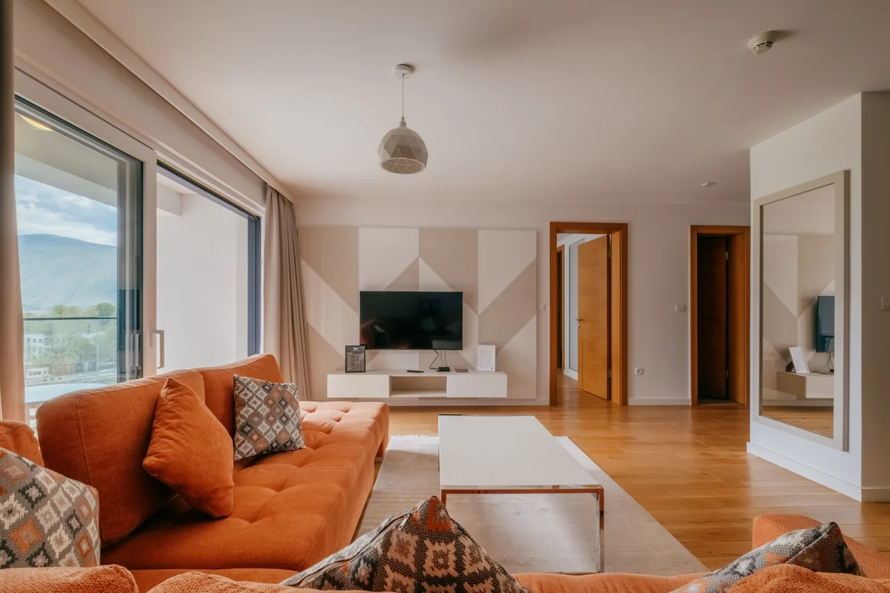 Living room — One-bedroom apartment. Orange sofa and cream kitchen