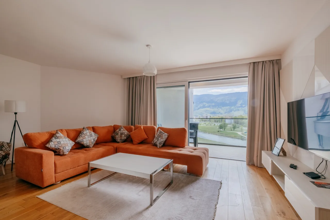 Living room — One-bedroom apartment. Orange sofa and cream kitchen